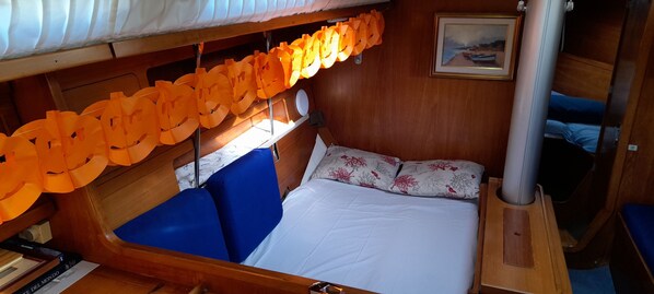 A cabin with a bed, blue upholstered seating, a wooden headboard, a white mattress, and a framed picture on the wall.