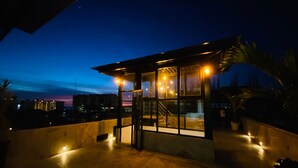 A modern building with a glass facade, a staircase, and a view of the cityscape at dusk. - A/C WIFI Zona Romantica Private Balcony Roof Top/Pool 5 Blocks from the beach (Puerto Vallarta)