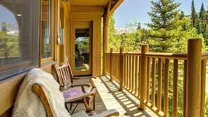 Eine Holzterrasse mit Glastür zu einem Raum, Holzstühle und Blick auf Bäume.