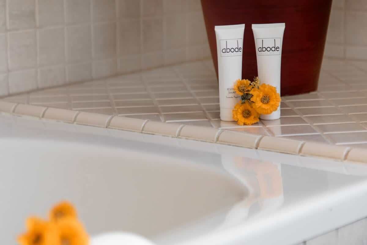 Dos tubos blancos con la marca 'abode' sobre una superficie de azulejos cerca de una bañera.