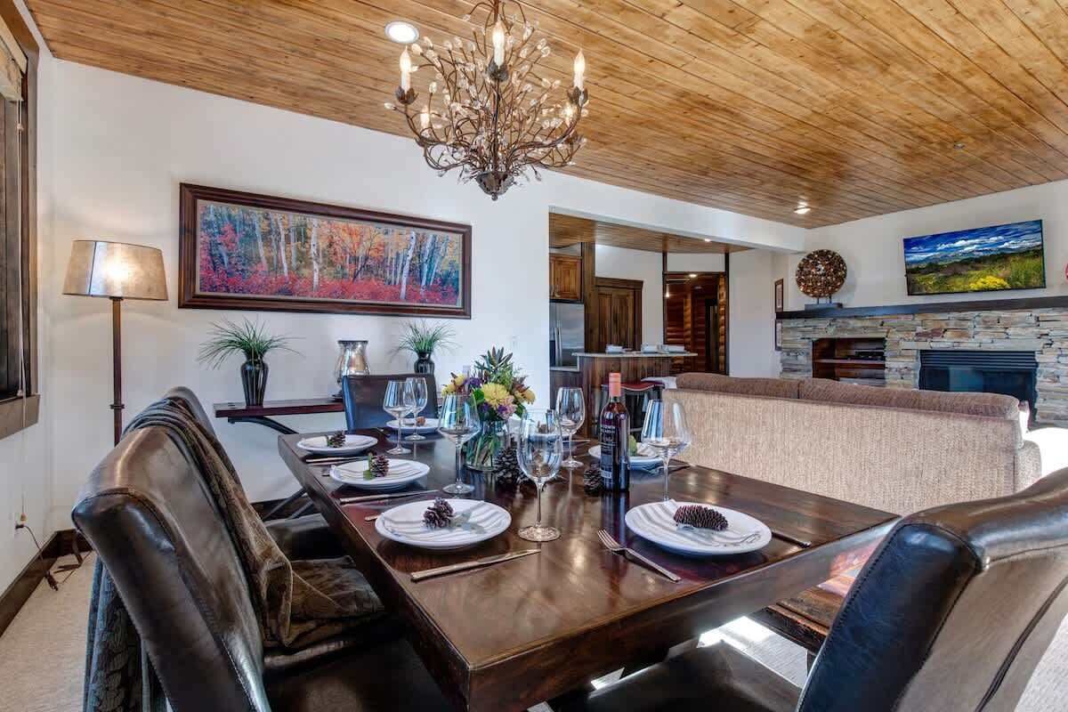 A dining area with a wooden table, leather chairs, a chandelier, and a painting on the wall.