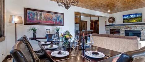 A dining area with a wooden table, leather chairs, a chandelier, and a painting on the wall.