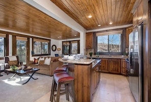 A spacious kitchen with wooden cabinets, a large island with stools, and a view of the outdoors.