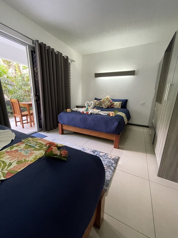 Habitación de hotel con dos camas, una mesa de comedor y vistas a la vegetación.