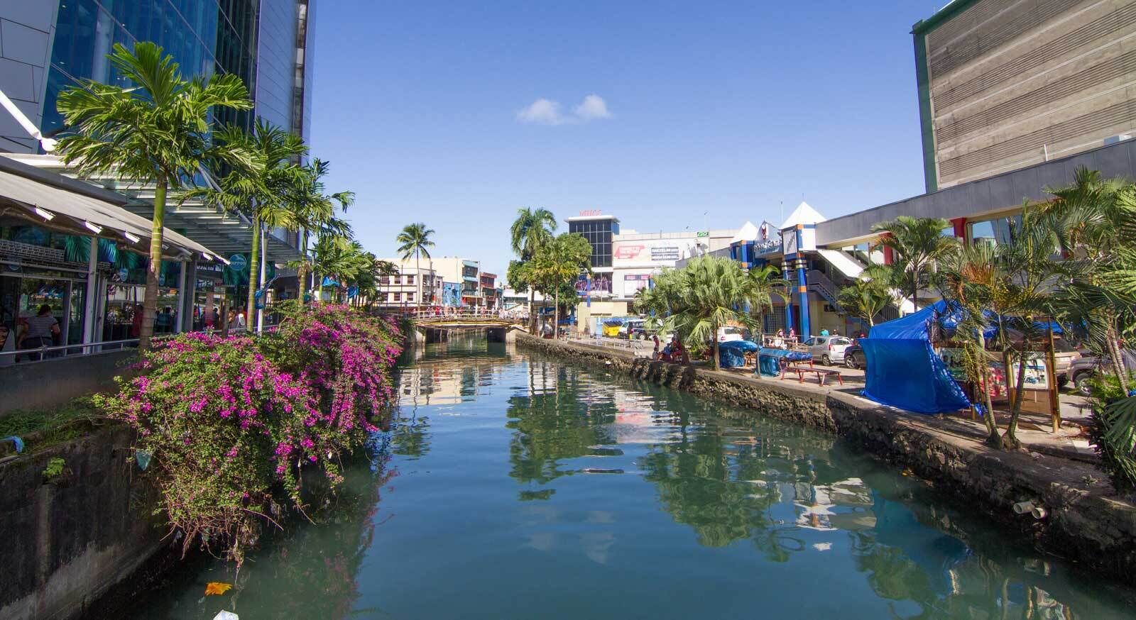 A canal with water, surrounded by buildings and palm trees.