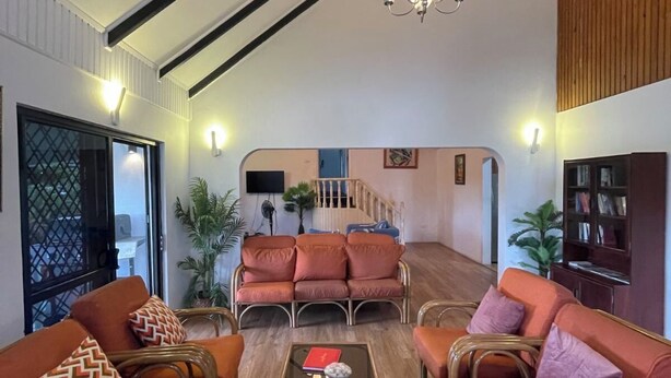 A spacious living room with high ceilings and exposed beams, furnished with orange sofas and wicker chairs, a central coffee table, and a chandelier. - Island Accommodation Suva Premier Hospitality (Suva)