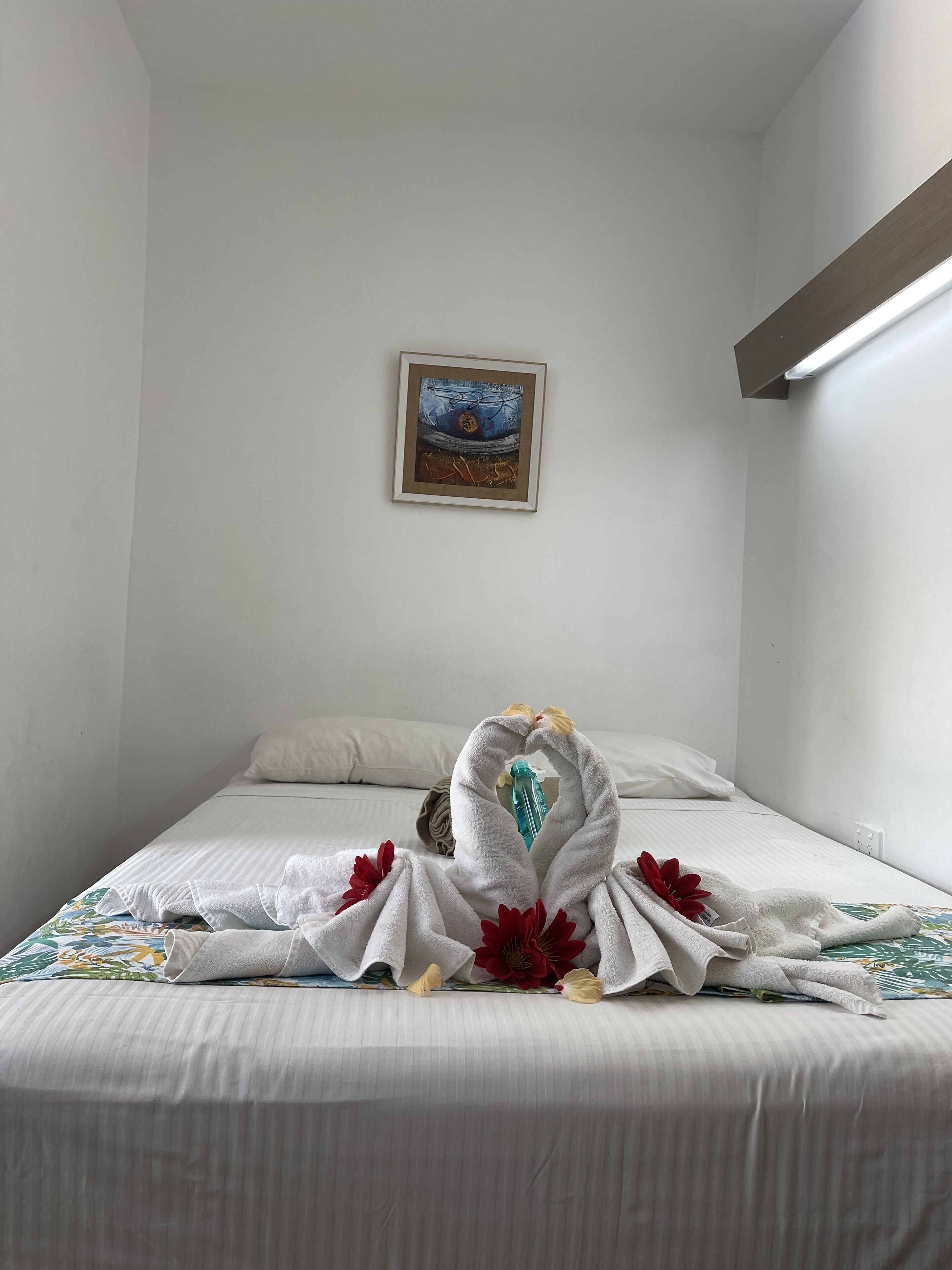 Una habitación de hotel con una cama bien tendida, un cuadro enmarcado en la pared y una lámpara.
