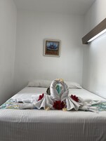 Una habitación de hotel con una cama bien tendida, un cuadro enmarcado en la pared y una lámpara.