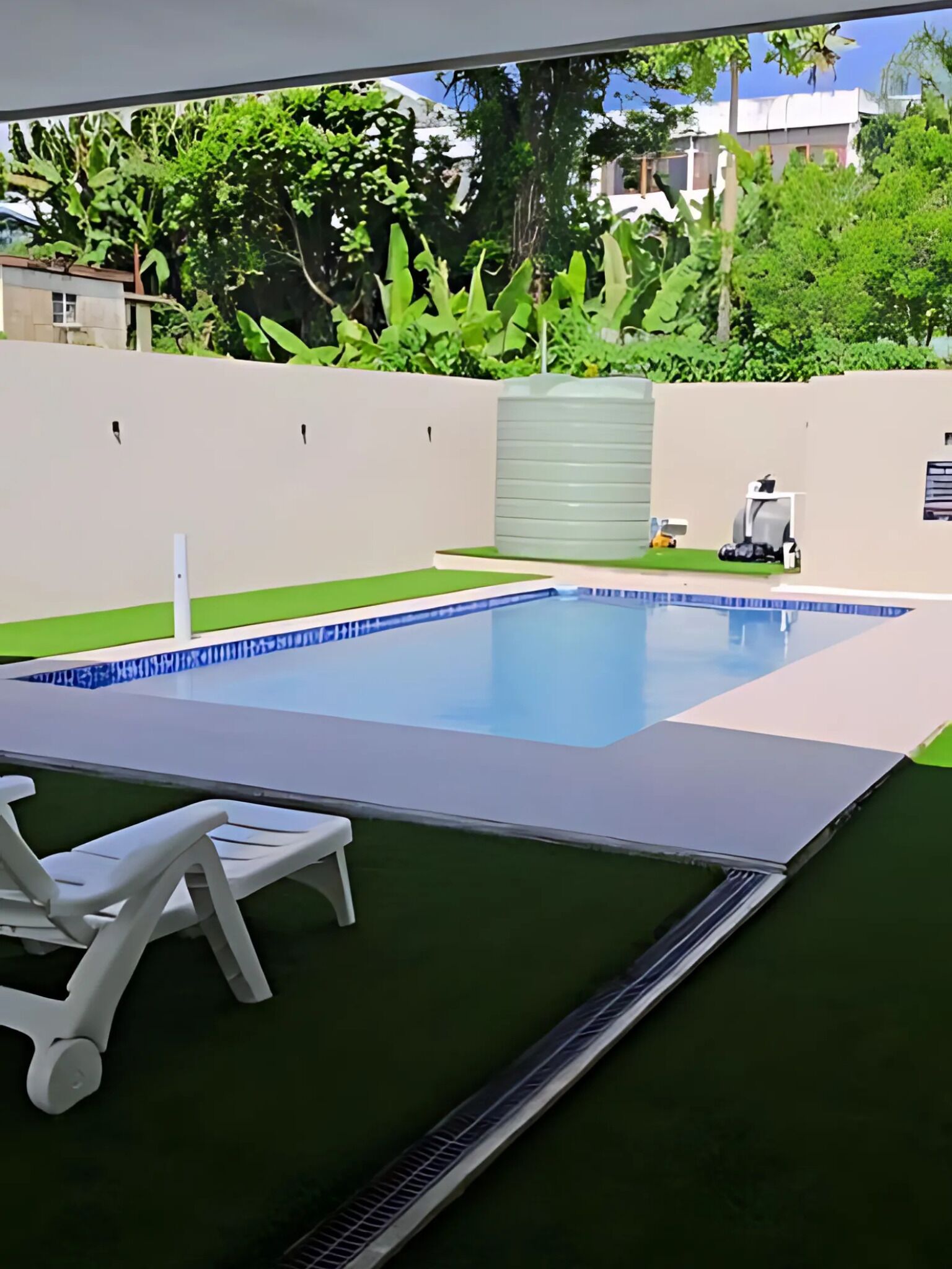 A swimming pool with a blue tiled edge, surrounded by a green lawn and white lounge chairs.