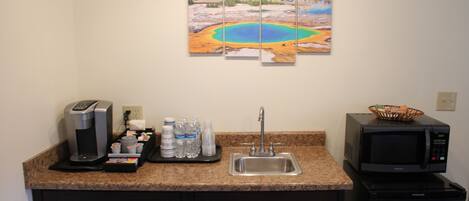 A kitchen with a coffee machine, water bottles, a sink, and a microwave.
