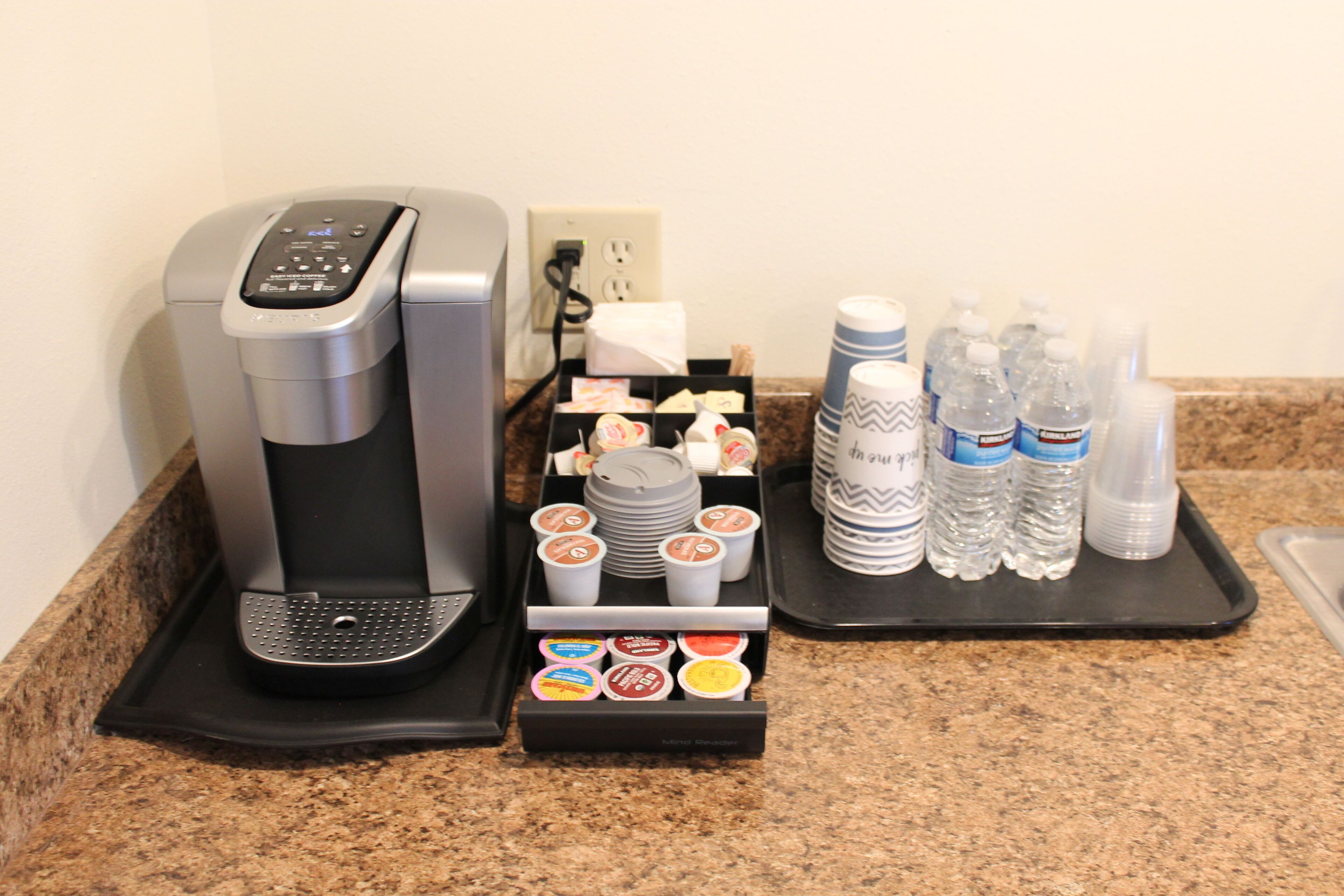 A coffee machine, a tray with disposable cups, and bottled water on a countertop.