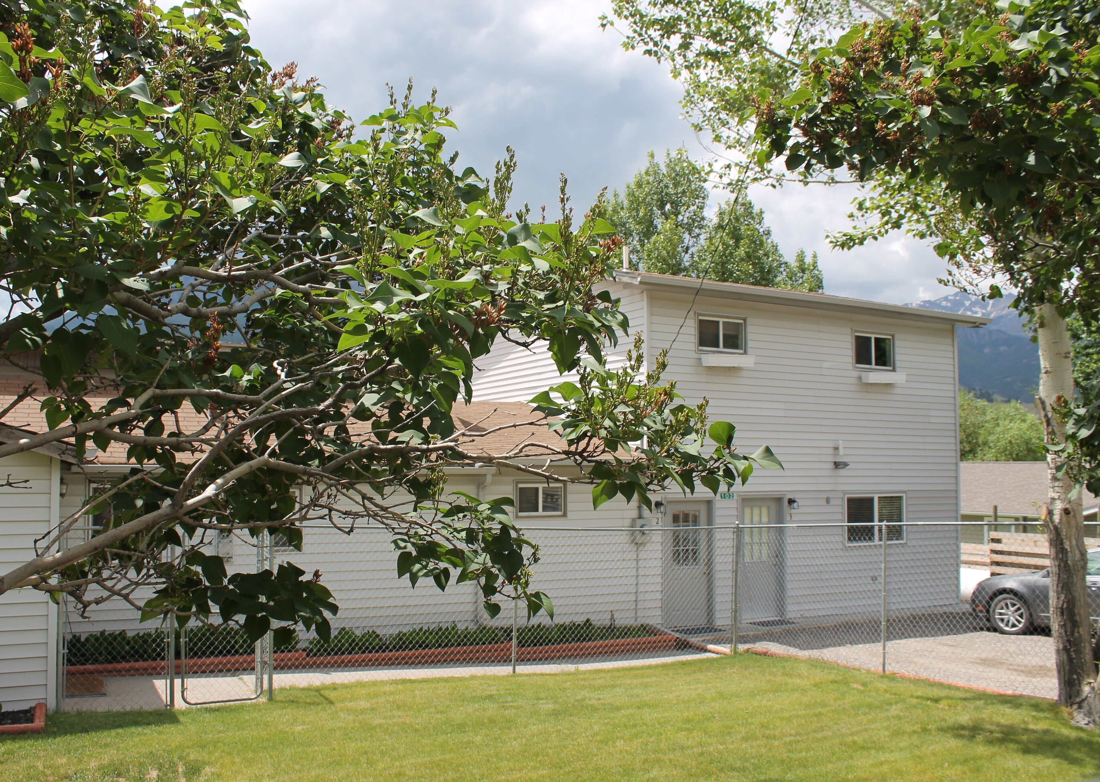 A two-story building with a fenced yard, a car parked outside, and a mountain in the background.