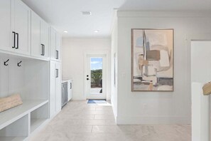 A modern hallway with white cabinetry, a large abstract painting on the wall, and a door leading to an outdoor area.