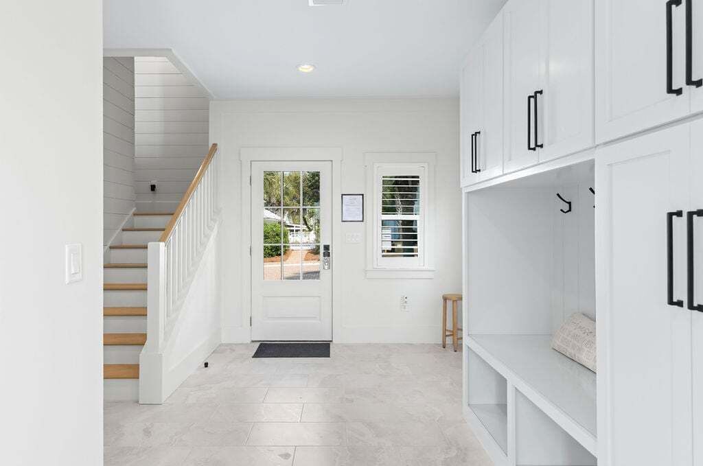 A clean, white interior with a staircase, a door with a window, and built-in cabinets.