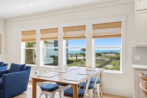 A modern dining area with a view of the beach and ocean, featuring a wooden table and blue cushioned chairs. - Blue Coast Bliss - 3BR/3.5BA Inlet Beach - Sleeps 6 - Gulf Views, Deeded Beach Access (Inlet Beach)
