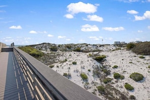 A wooden boardwalk leading to a beach with dunes and sparse vegetation.