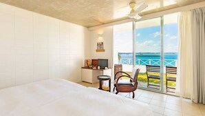 A hotel room with a large bed, a desk with a TV, and a view of the sea through a sliding glass door. - 413 Hamahiga Hotel&cafe (Uruma)