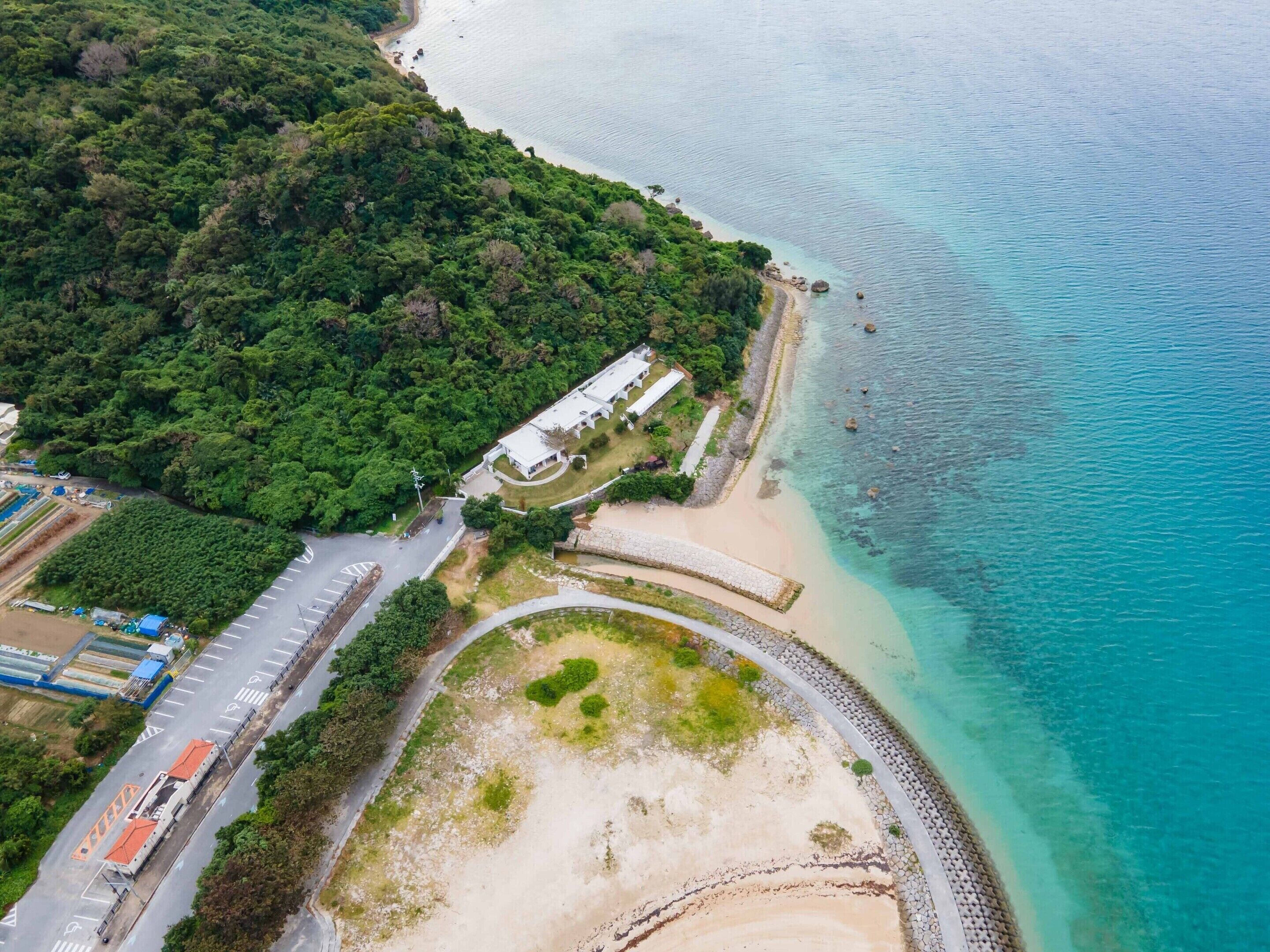 An aerial view of a coastal area with a road, a parking lot, and a building adjacent to the beach.