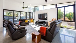 A modern living room with a large TV, leather sofas, and a ceiling fan. - Chesters by the Bay: luxury family home, walk to beach and town (Dunsborough)