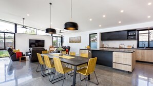 A modern kitchen with a central island, dining area with chairs, and a large window. - Chesters by the Bay: luxury family home, walk to beach and town (Dunsborough)