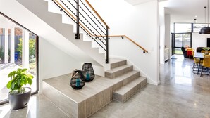 A modern staircase with a wooden handrail, leading to a bright room with a dining area and a large window. - Chesters by the Bay: luxury family home, walk to beach and town (Dunsborough)