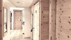 A hallway with wooden walls, a door with a coat rack, and a kitchen area in the background. - Nr.15A Apartment ZIRBENzeit - Guesthouse - Apart Braito (Grän)