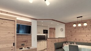 A modern kitchen with wooden paneling, a dining area with a table and chairs, and a TV mounted on the wall. - Nr.15A Apartment ZIRBENzeit - Guesthouse - Apart Braito (Grän)