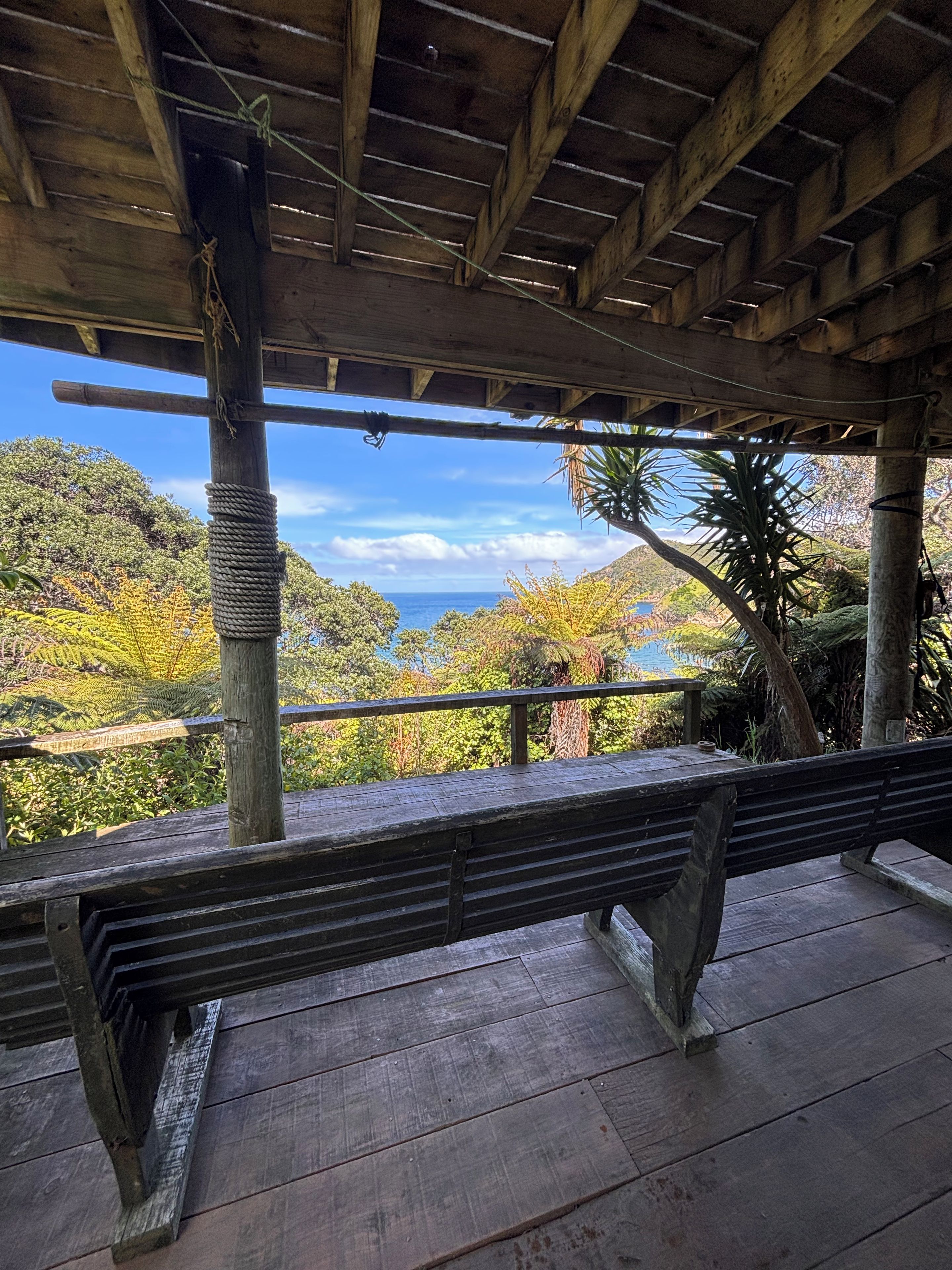 A wooden bench under a covered area with a view of a mountainous landscape and the sea.