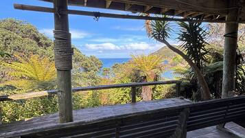 A wooden bench under a covered area with a view of a mountainous landscape and the sea.