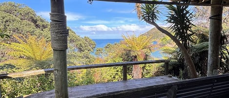Un banc en bois, placé sous un espace abrité, d’où l’on peut admirer un paysage montagneux et la mer.