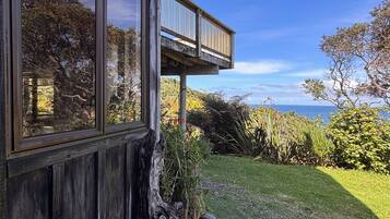 A house with a large window and a balcony overlooking a grassy area with a view of the ocean.
