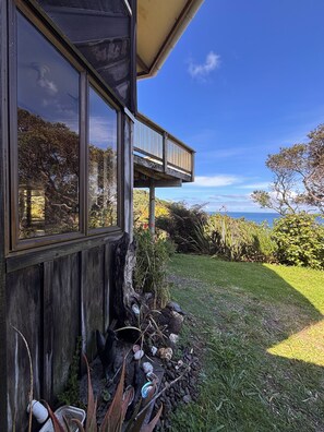 Une maison dotée d’une grande fenêtre et d’un balcon donnant sur un espace verdoyant, avec vue sur l’océan.