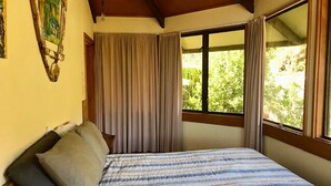 Une chambre à coucher avec un lit, des rideaux et une fenêtre donnant sur un paysage verdoyant.