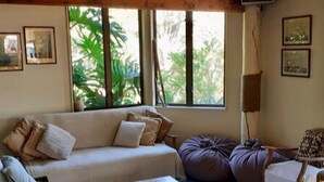 Un salon avec un canapé, une table basse et un fauteuil en forme de poire. De grandes fenêtres offrent une vue sur la verdure environnante.