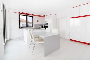 A modern kitchen with white cabinetry, a large island, and a red accent wall.