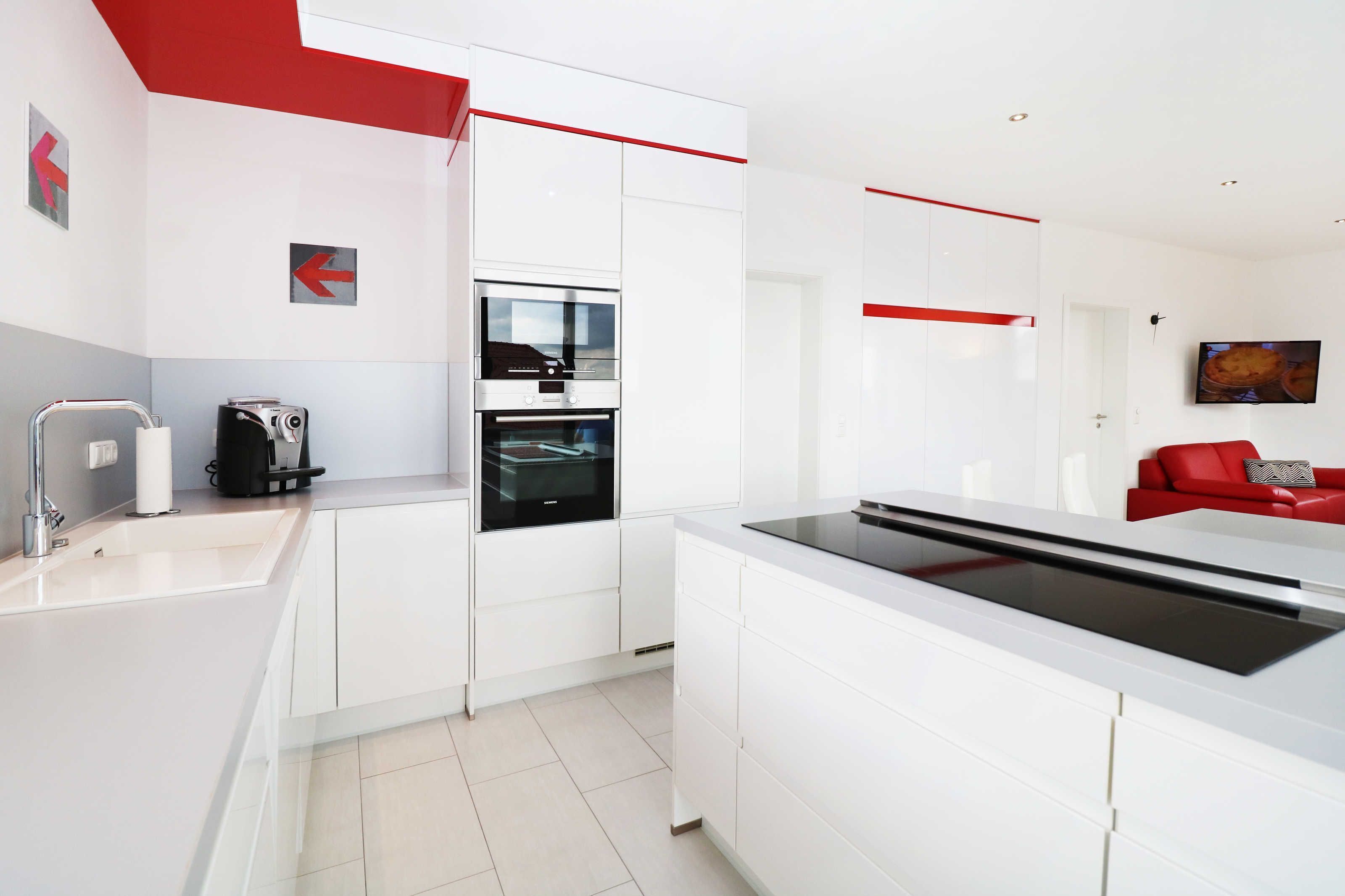 A modern kitchen with white cabinetry, a built-in oven, and a red accent wall.