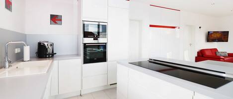 A modern kitchen with white cabinetry, a built-in oven, and a red accent wall.