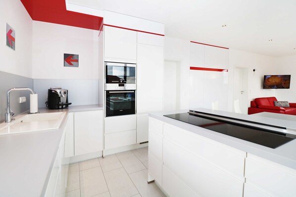 Una cocina moderna con armarios blancos, horno integrado y una pared de acento roja.