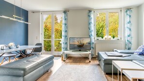 A modern living room with a grey sofa, a dining table, and a TV. - Ferienhaus Ivory, Deutschland (Binz)