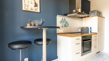 A compact kitchen with a bar stool, a microwave, and a stove.