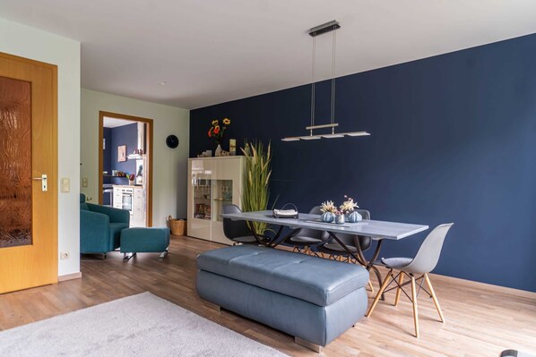 A modern living room with a dining area, featuring a sofa, ottoman, and a dining table with chairs.