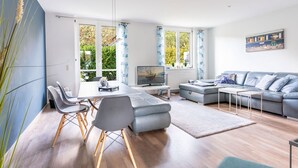 A modern living room with a dining area, large windows, and a grey sofa. - Ferienhaus Ivory, Deutschland (Binz)