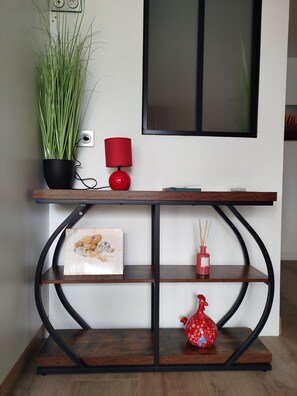 Una consola de madera con una planta en maceta, una lámpara roja, un cuadro enmarcado y un jarrón decorativo.