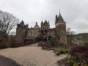 A historic castle with a central tower, a large courtyard, and a wooden bridge leading to the entrance.