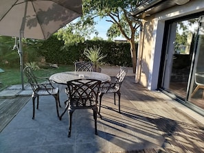 An outdoor patio with a round table and chairs, surrounded by a wooden deck and a garden.