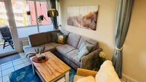 A living room with a sofa, a wooden coffee table, a wicker chair, and a painting on the wall.