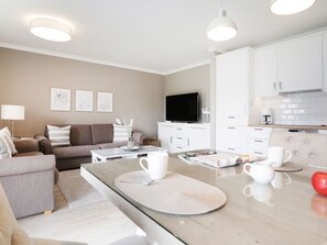 Una sala de estar moderna con sofá, una mesa de centro y una zona de cocina con armarios y televisor.