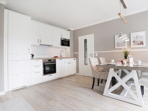 Una cocina moderna con armarios blancos, microondas, horno y un comedor con mesa y sillas de vidrio.