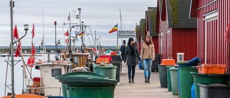 Une jetée en bois, avec des bateaux et des poubelles, qui mène à un bâtiment rouge sur lequel est apposée une enseigne.