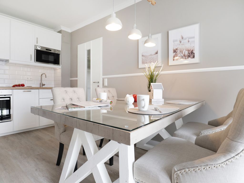 Una cocina moderna con armarios blancos, una mesa de comedor de vidrio y una silla tapizada en tono beige.
